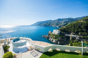 Una terrazza sul mare con un'area salotto circolare, un edificio bianco con un balcone e vista mare e monti.