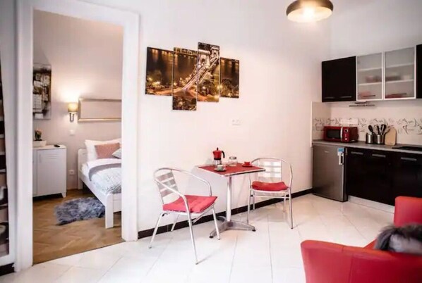 A compact living space with a kitchenette, a dining area with two chairs, a bed, and a wall-mounted artwork. - Lovely, compact quiet flat in the center (Nari's) (Budapest)