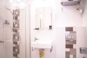 A bathroom with a glass shower enclosure, a white sink, and a mirror above it. - Lovely, compact quiet flat in the center (Nari's) (Budapest)