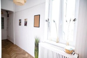 Un pasillo con un radiador blanco, una ventana con vistas e imágenes enmarcadas en la pared.