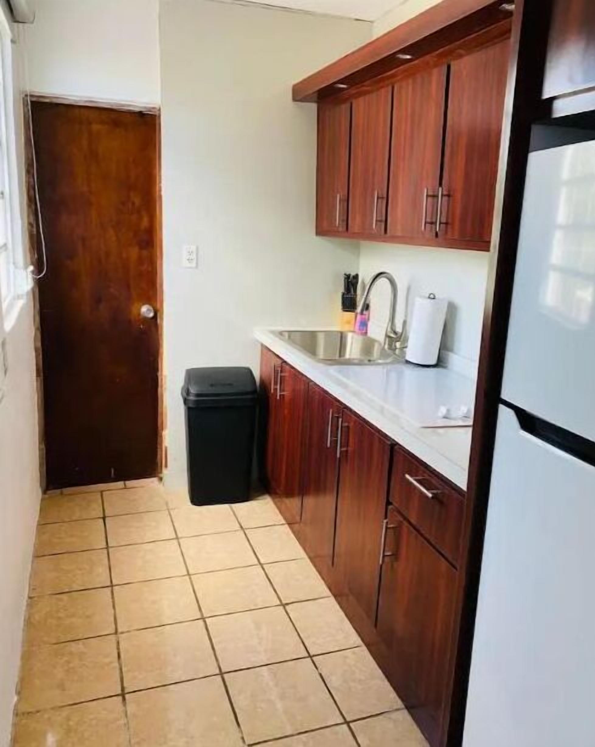 A compact kitchen with wooden cabinets, a stainless steel sink, and a black trash bin.