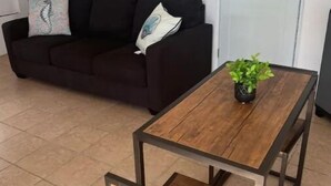 Uma sala de estar com um sofá marrom escuro, uma mesa de centro de madeira e uma pequena planta em vaso.