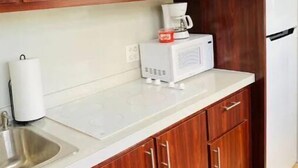 Cozinha com armários de madeira, bancada branca, cafeteira e micro-ondas.