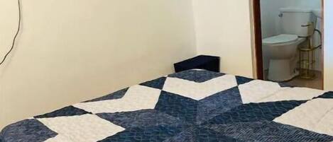 A bedroom with a bed, a television mounted on the wall, and a door leading to a bathroom.