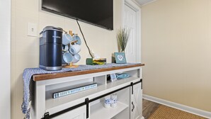 Una kitchenette con cafetera, tazas y un cuadro en un estante.
