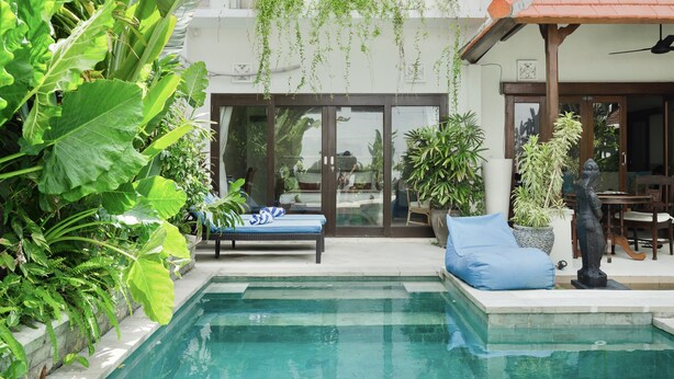 A pool area with a lounge chair and a statue, surrounded by lush greenery and a building with a tiled roof. - Villa Carissa: Private Pool in Seminyak Center, Bali (Bali)