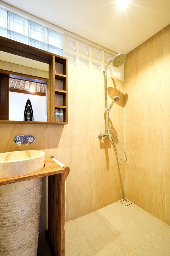 A bathroom with a wooden vanity, a round sink, a mirror, and a shower with a handheld showerhead.