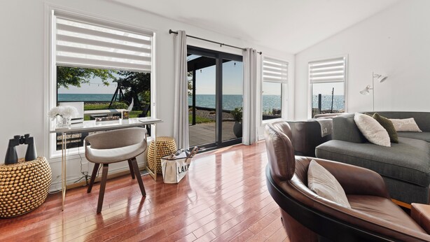 Una sala de estar moderna con vista al mar, un sofá, una silla y un escritorio con una computadora portátil.