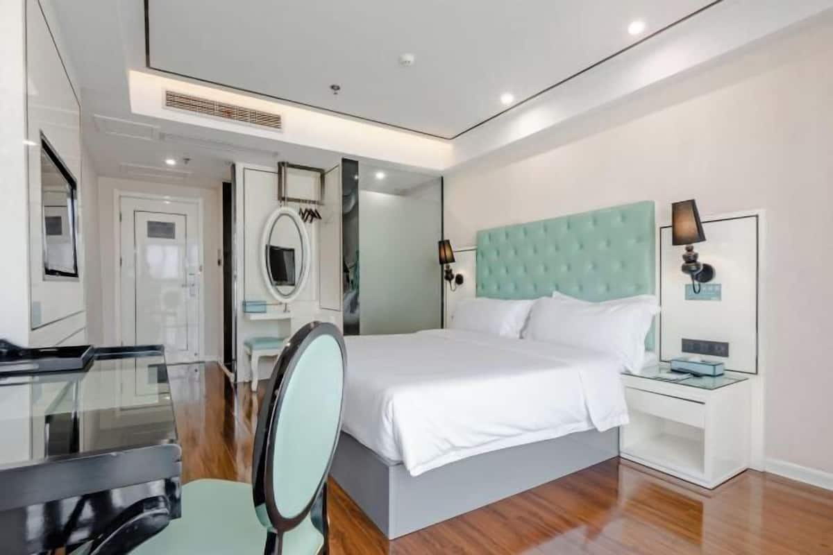 Habitació d'hotel moderna amb llit, escriptori, cadira, mirall i taula de nit.