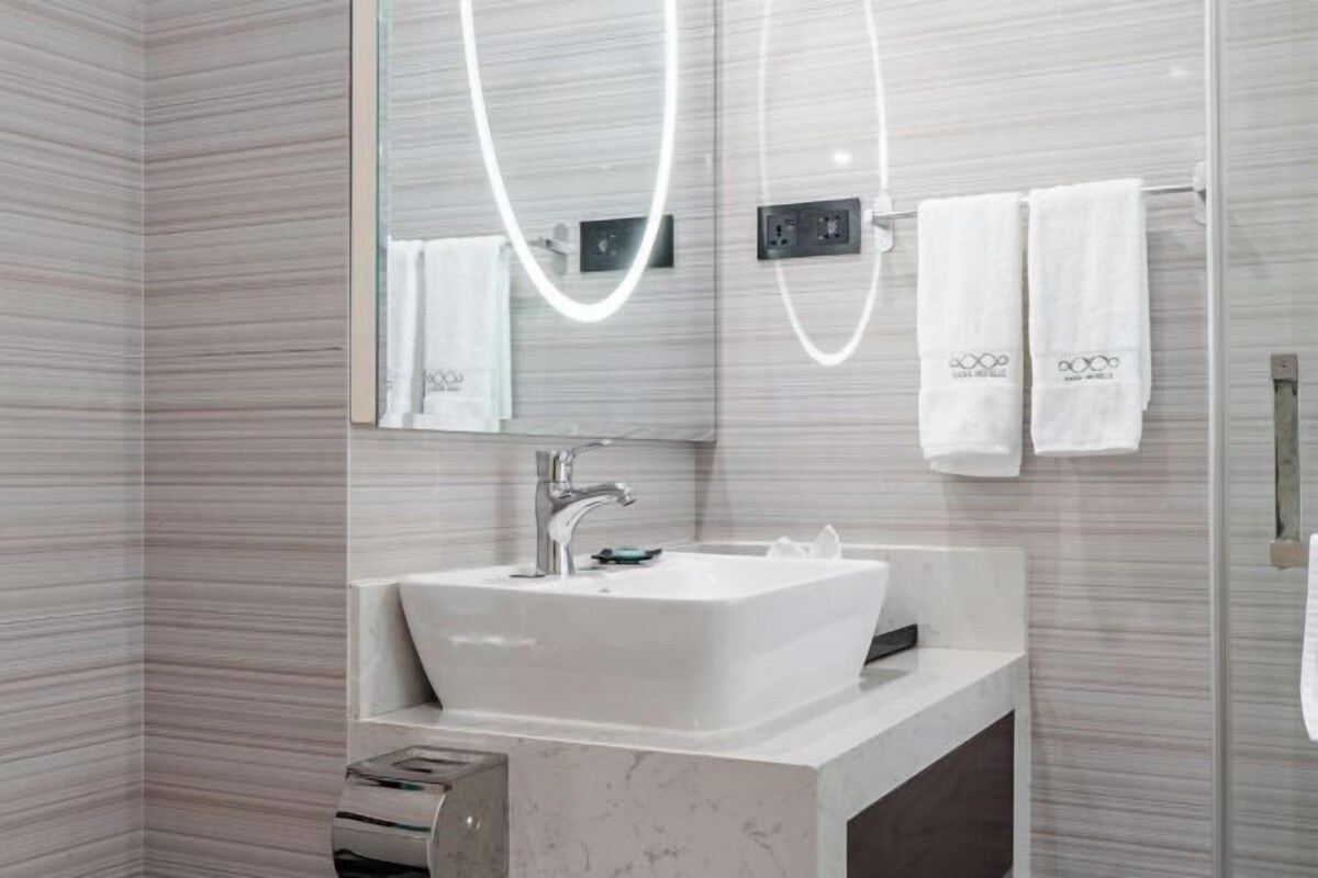 Casa de banho moderna com lavatório branco, espelho e porta-toalhas.