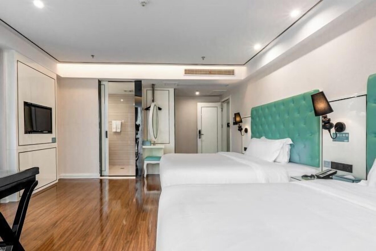 A hotel room with two beds, a TV, a desk, and a bathroom visible through an open door.