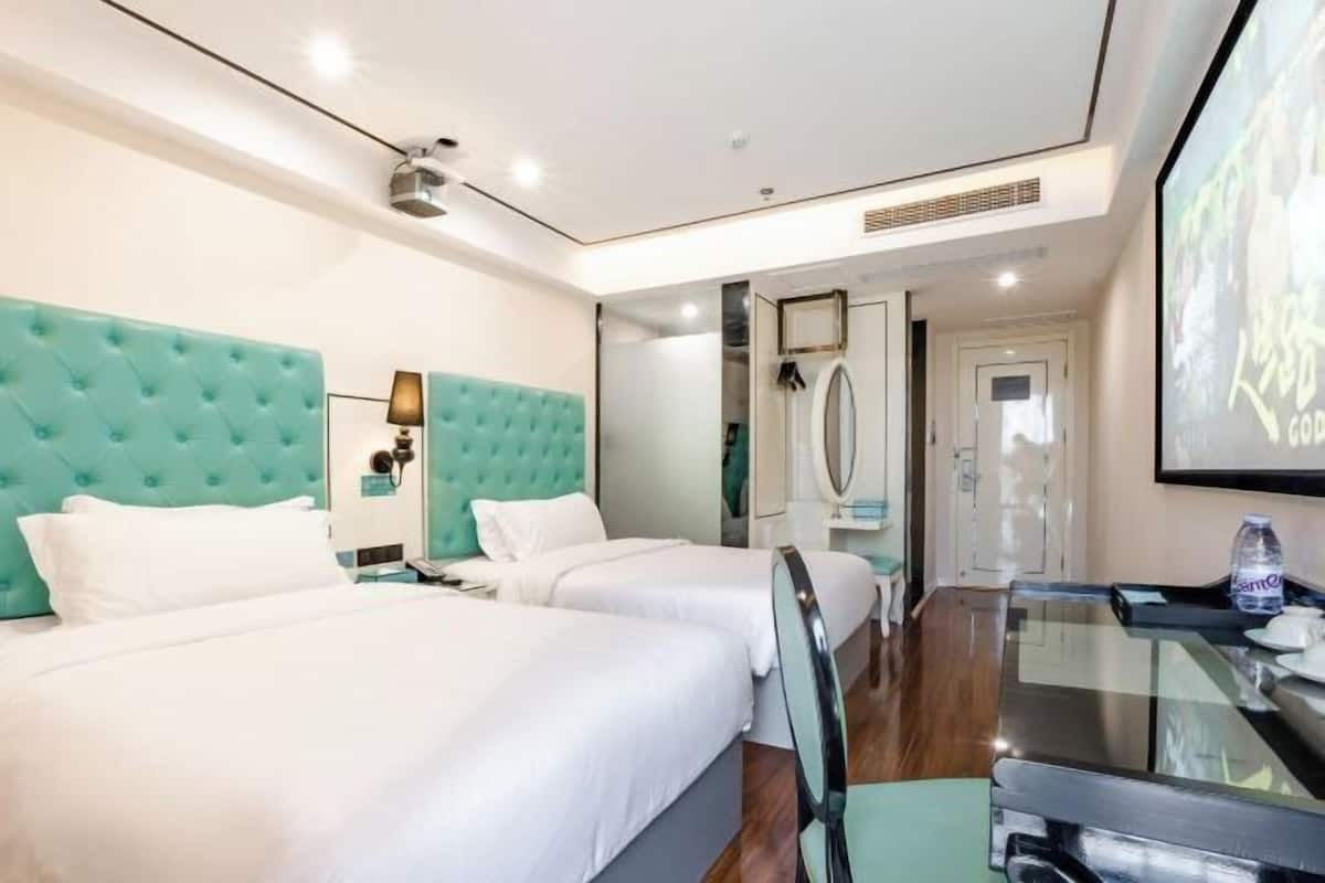 Habitació d'hotel amb dos llits, una taula de vidre, un minibar i un gran pantalla penjada a la paret.