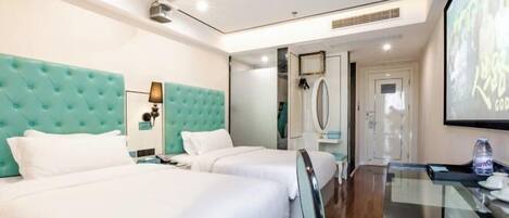 A hotel room with two beds, a glass table, a minibar, and a large screen on the wall.