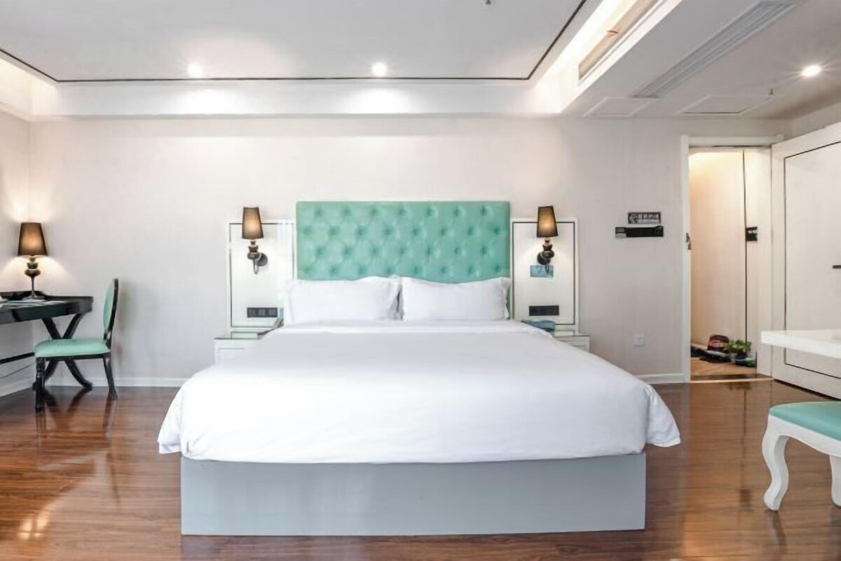 Quarto de hotel bem arrumado com uma cama grande, duas mesas de cabeceira com abajures, uma cadeira e uma mesinha.