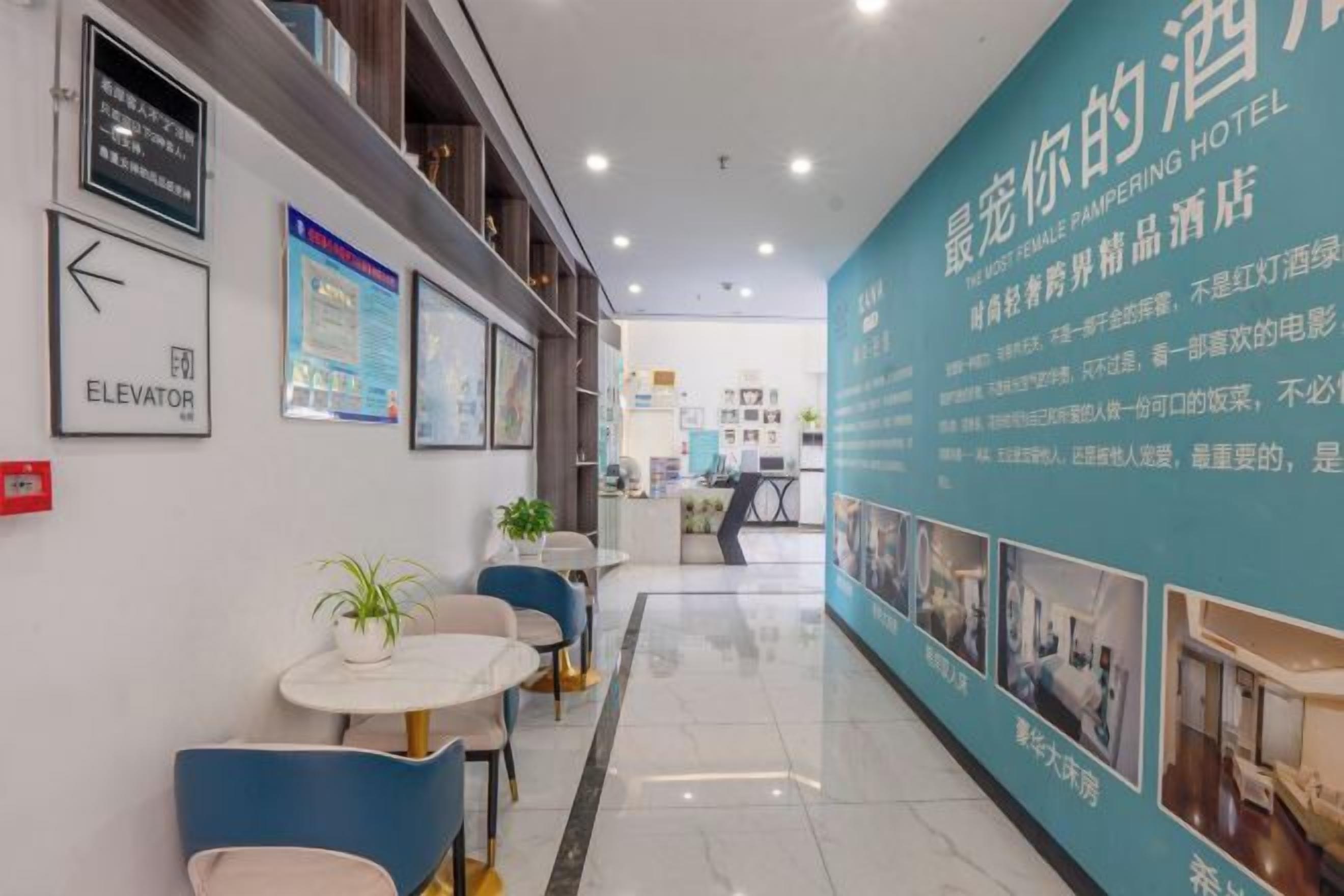 A hotel corridor with a reception desk, seating area, and directional signs.