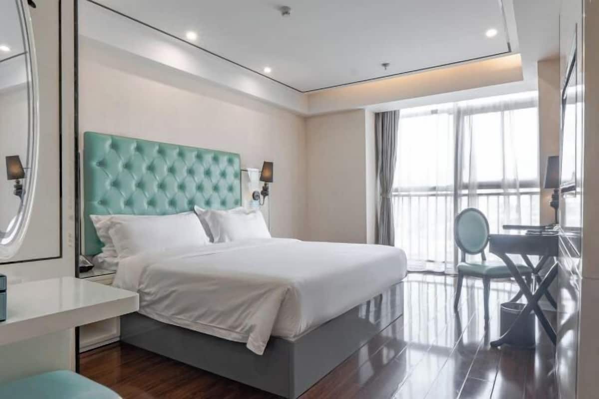 Habitació d'hotel moderna amb un llit gran, un escriptori, una cadira i una finestra amplia.