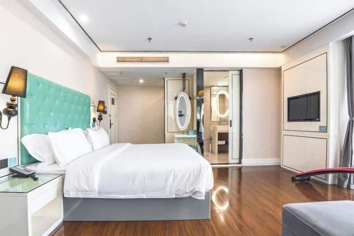 Habitació d'hotel moderna amb llit, taulella de nit, mirall, tocador i televisió.