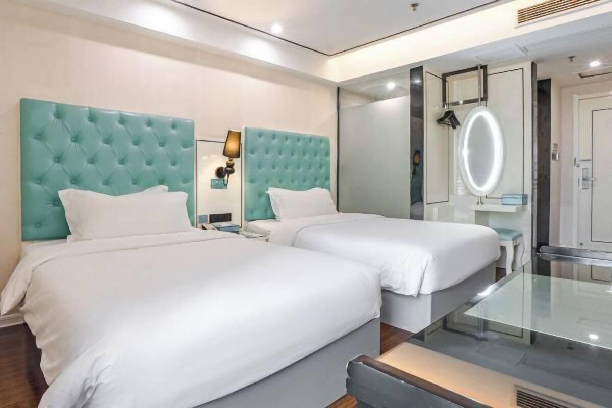 Habitació d'hotel amb dos llits, una taula de vidre, un bany amb mirall i una petita zona de seients.