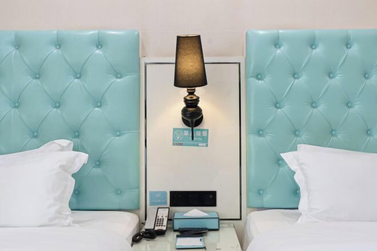 Quarto de hotel com duas camas, cada uma com cabeceira estofada, mesa de cabeceira com abajur, telefone e caixa de lenços.