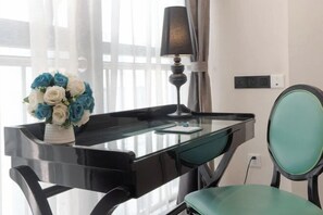 Quarto moderno com escrivaninha de vidro, luminária, cadeira e um vaso de flores.