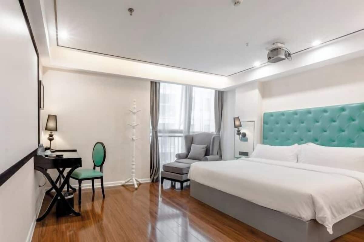 Habitació d'hotel amb un llit, escriptori, cadira, làmpada de peu i finestra.