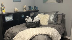 A bedroom with a large bed, a nightstand, a dresser, and a wall with a beach-themed sign and artwork. - Charming Home just minutes from Interstate and Mall (Kevil)