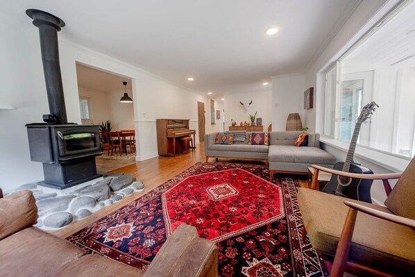 A living room with a stone fireplace, a red patterned rug, a grey sofa, and a guitar.