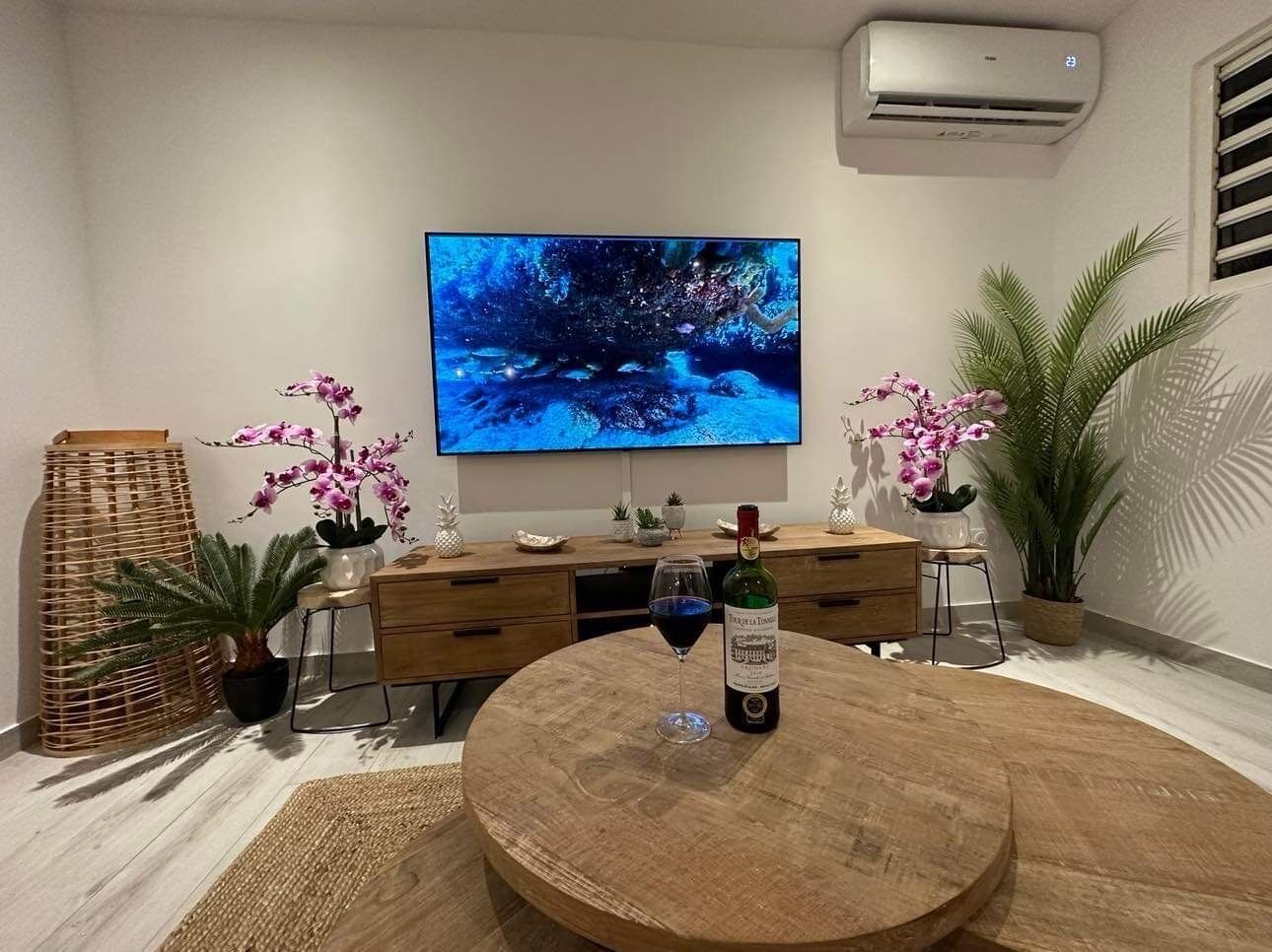 Een moderne woonkamer met een houten salontafel, een flatscreen televisie aan de muur, een fles wijn en potorkideeën.