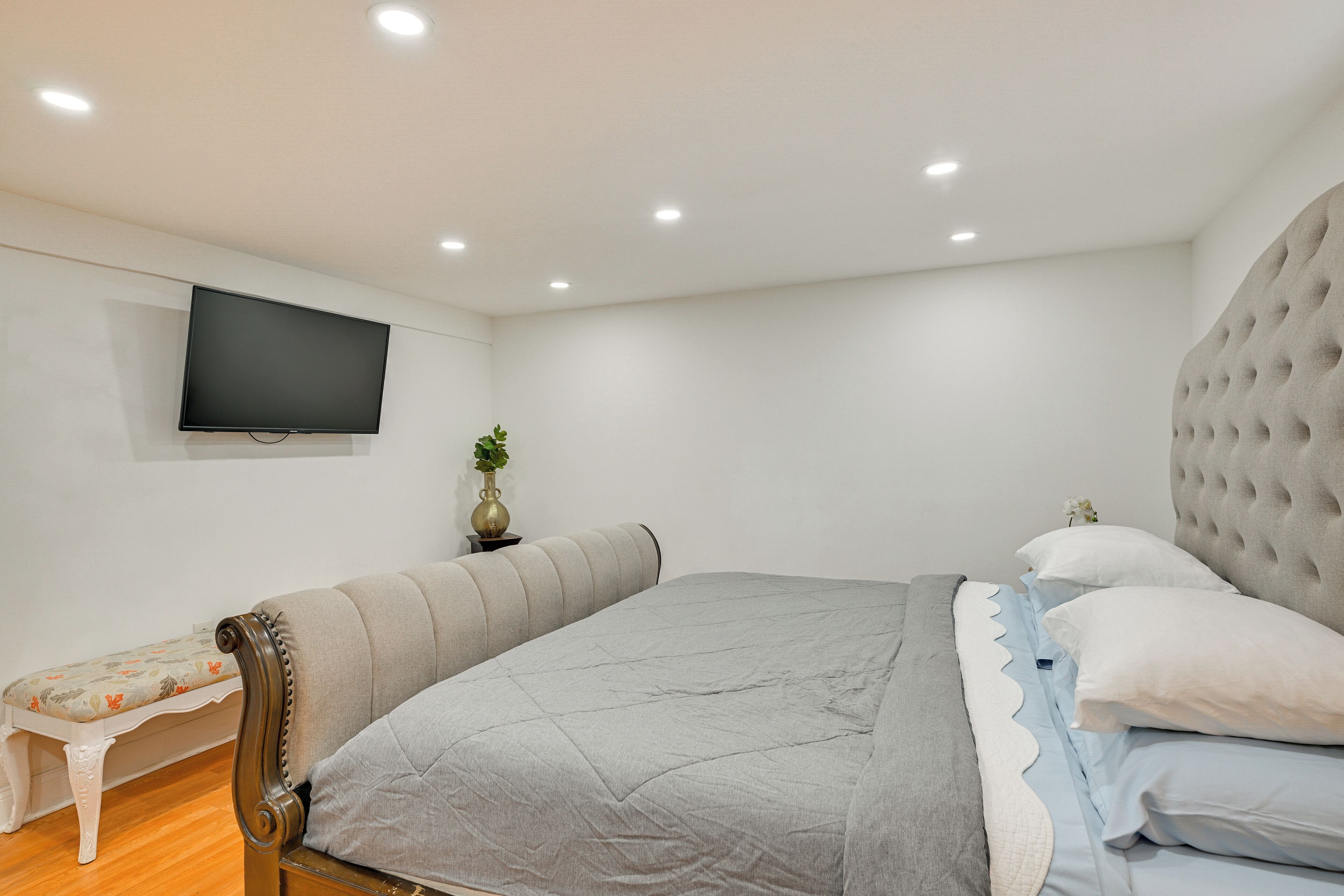 A bedroom with a bed, a bench, a television, and a wall-mounted plant.