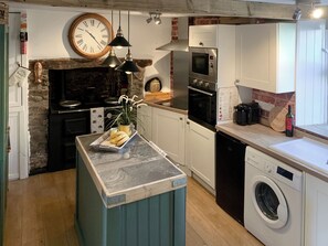 A compact kitchen with a central island, a built-in oven, a washing machine, and a clock on the wall.