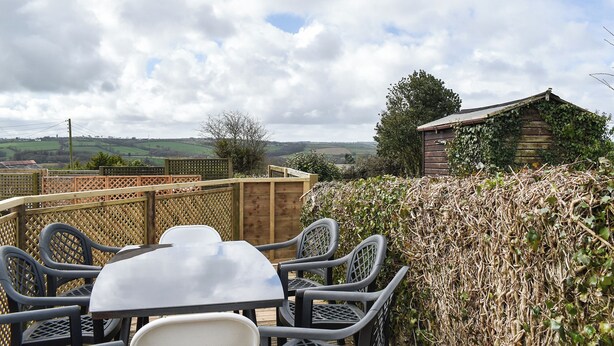An outdoor dining area with a table and chairs, surrounded by a wooden fence and a hedge. - Only 4 miles from Westward Ho. (Littleham, near Bideford)