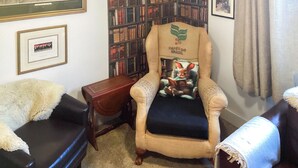 A cozy room with a leather sofa, a plush armchair with a print, a bookshelf, and framed pictures on the walls. - Only 4 miles from Westward Ho. (Littleham, near Bideford)
