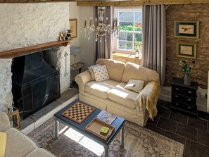 A cozy living room with a fireplace, a sofa, a coffee table with a chessboard, and a stone wall.