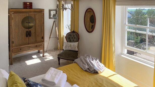 A bedroom with a bed, a wooden wardrobe, a chair, a window with a view, and a mirror on the wall. - Only 4 miles from Westward Ho. (Littleham, near Bideford)