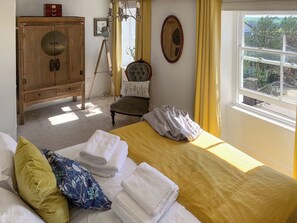 A bedroom with a bed, a wooden wardrobe, a chair, a window with a view, and a mirror on the wall.