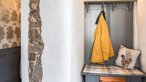 A room with a stone wall, a bench with a checkered cushion, a yellow jacket hanging, and a pillow with a bird design. - Only 4 miles from Westward Ho. (Littleham, near Bideford)