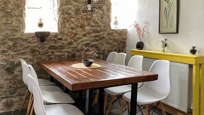 A dining area with a wooden table, white chairs, a stone wall, and a yellow cabinet. - Only 4 miles from Westward Ho. (Littleham, near Bideford)