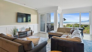 Una sala de estar con un televisor grande, dos sofás, una mesa de centro y vista a la playa.