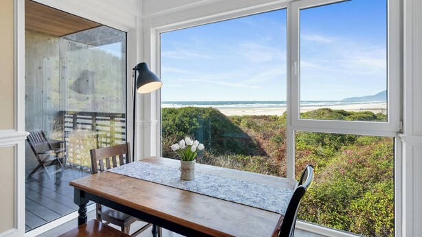 Un comedor con una mesa, sillas, una lámpara y vistas a la playa y al océano a través de amplias ventanas.