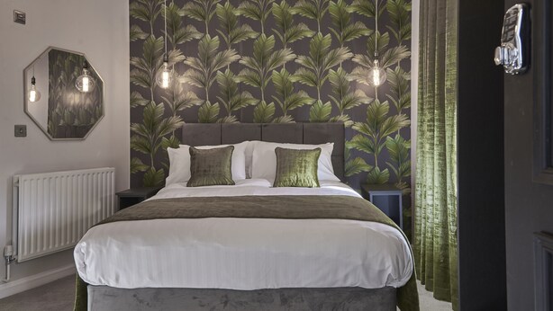 A bedroom with a large bed, a headboard, a mirror, and a wall with a leaf pattern. - Home at Tancred Road  (Liverpool)