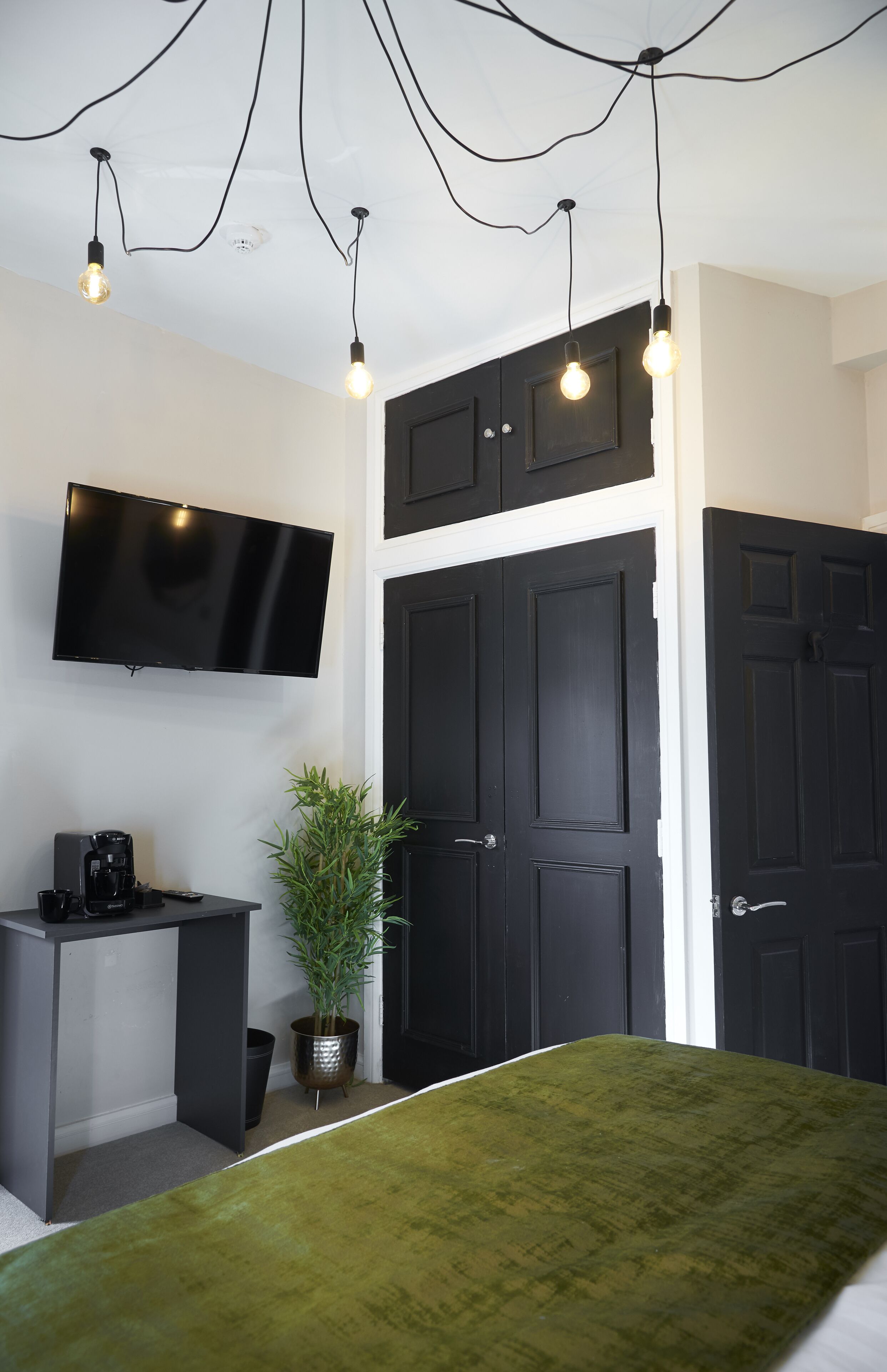 A room with a bed, a desk, a television, and black doors.