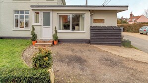 Una casa a due piani con un portico anteriore, un piccolo giardino e un'auto parcheggiata nel vialetto.