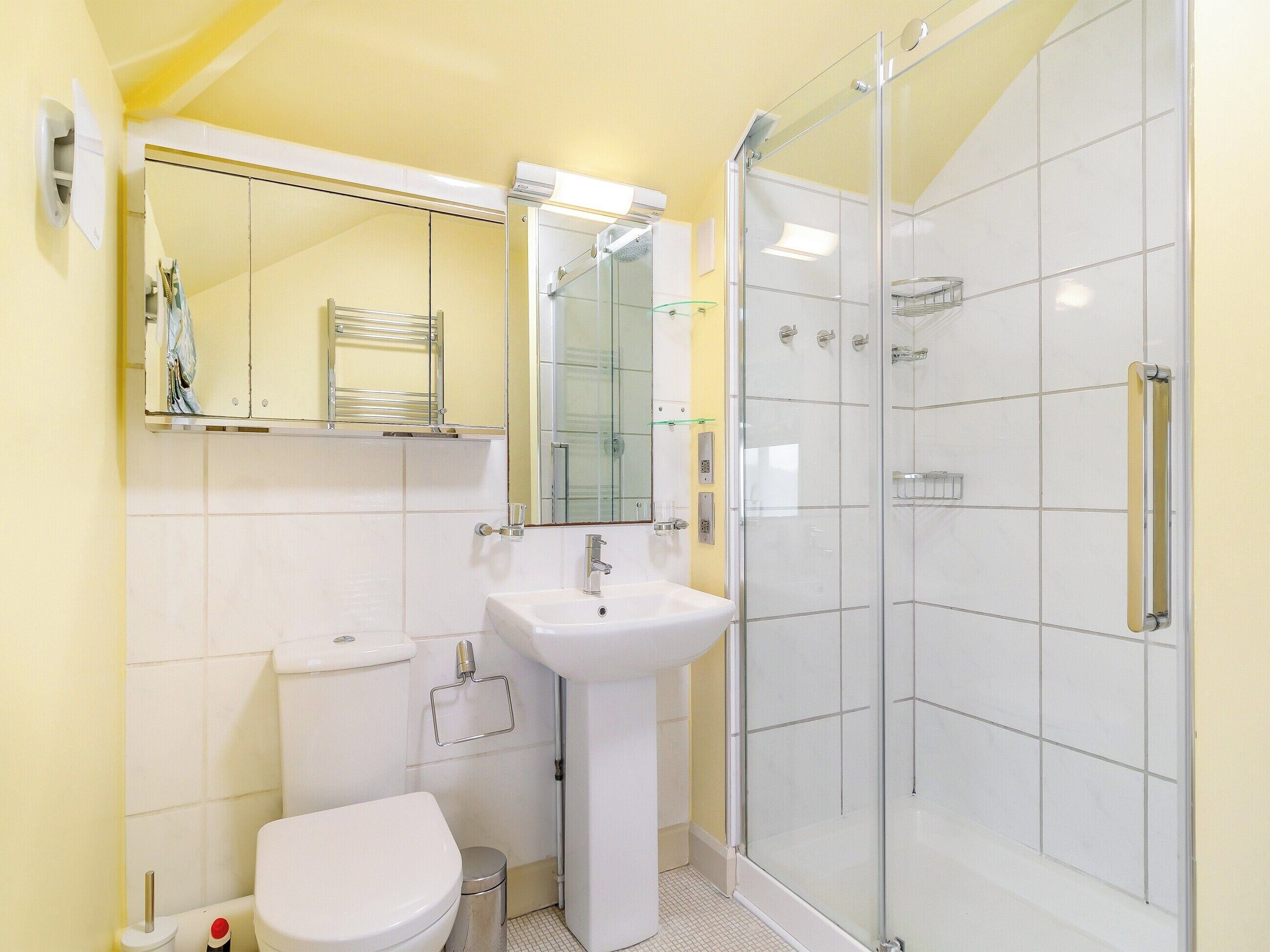 Et badeværelse med toilet, håndvask og brusekabine med glasvægge.