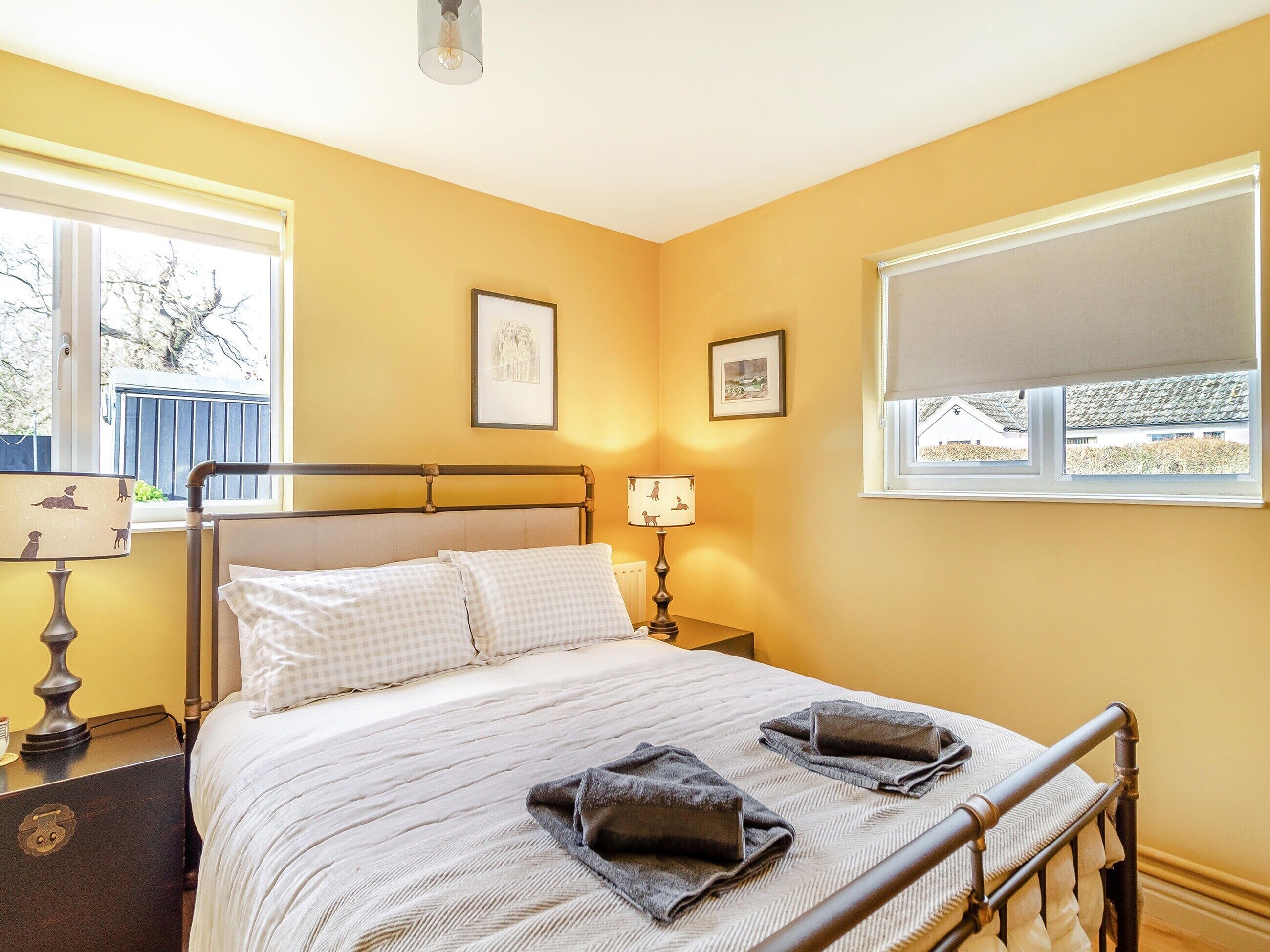 Un dormitorio con cama, mesitas de noche, lámpara y ventana con vistas al exterior.