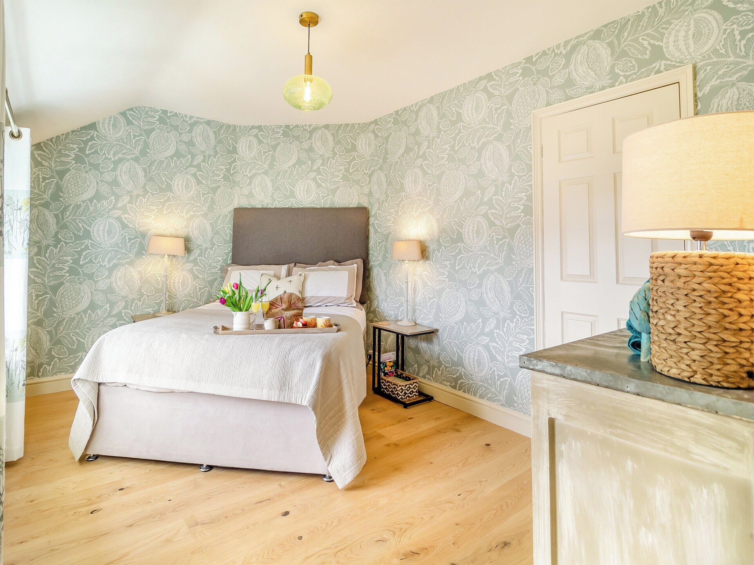 A bedroom with a bed, bedside lamps, a bedside table with a lamp, and a tray with breakfast items.