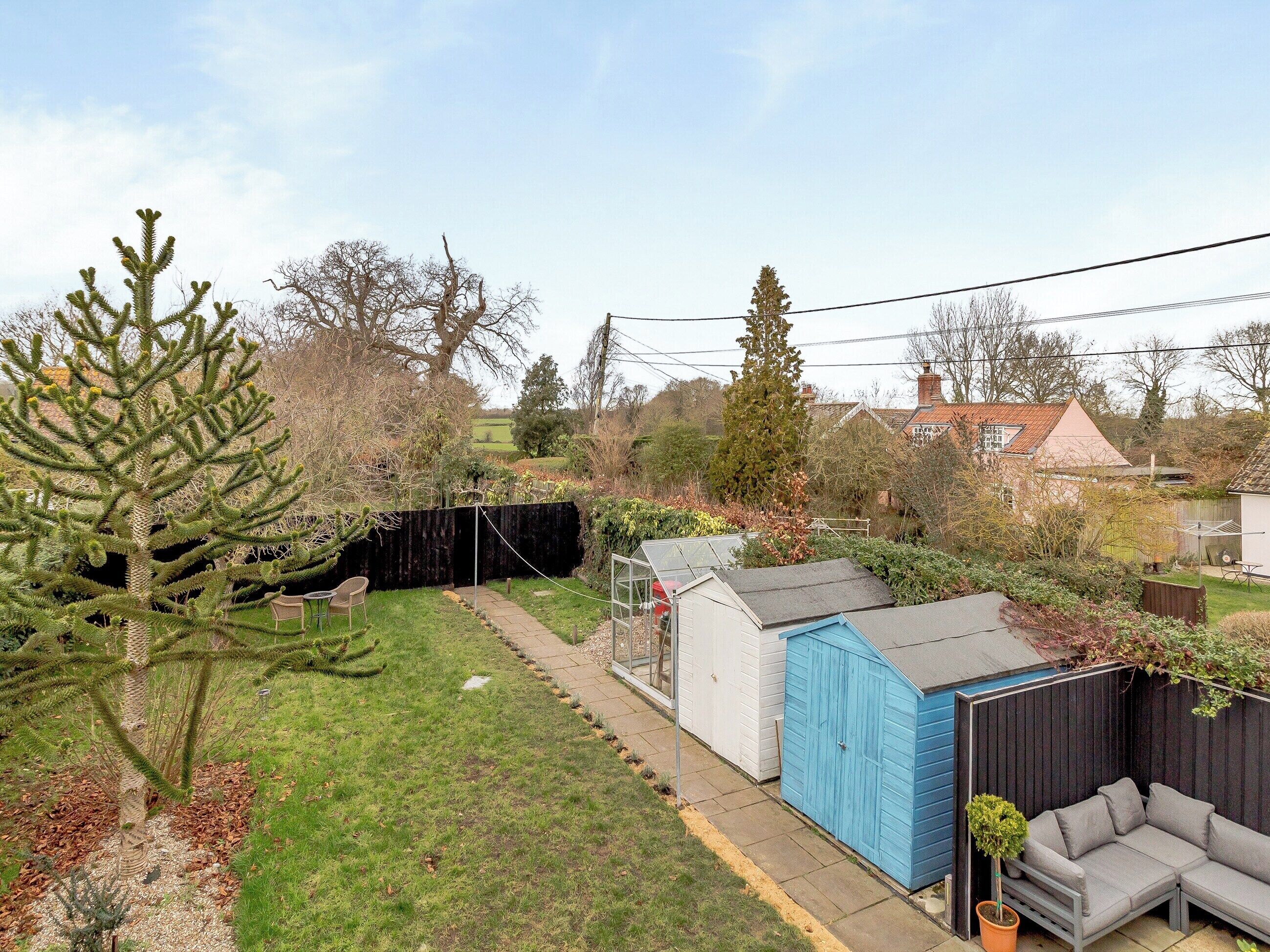 A backyard with a small shed, a blue storage box, a grey outdoor sofa, and a potted plant.