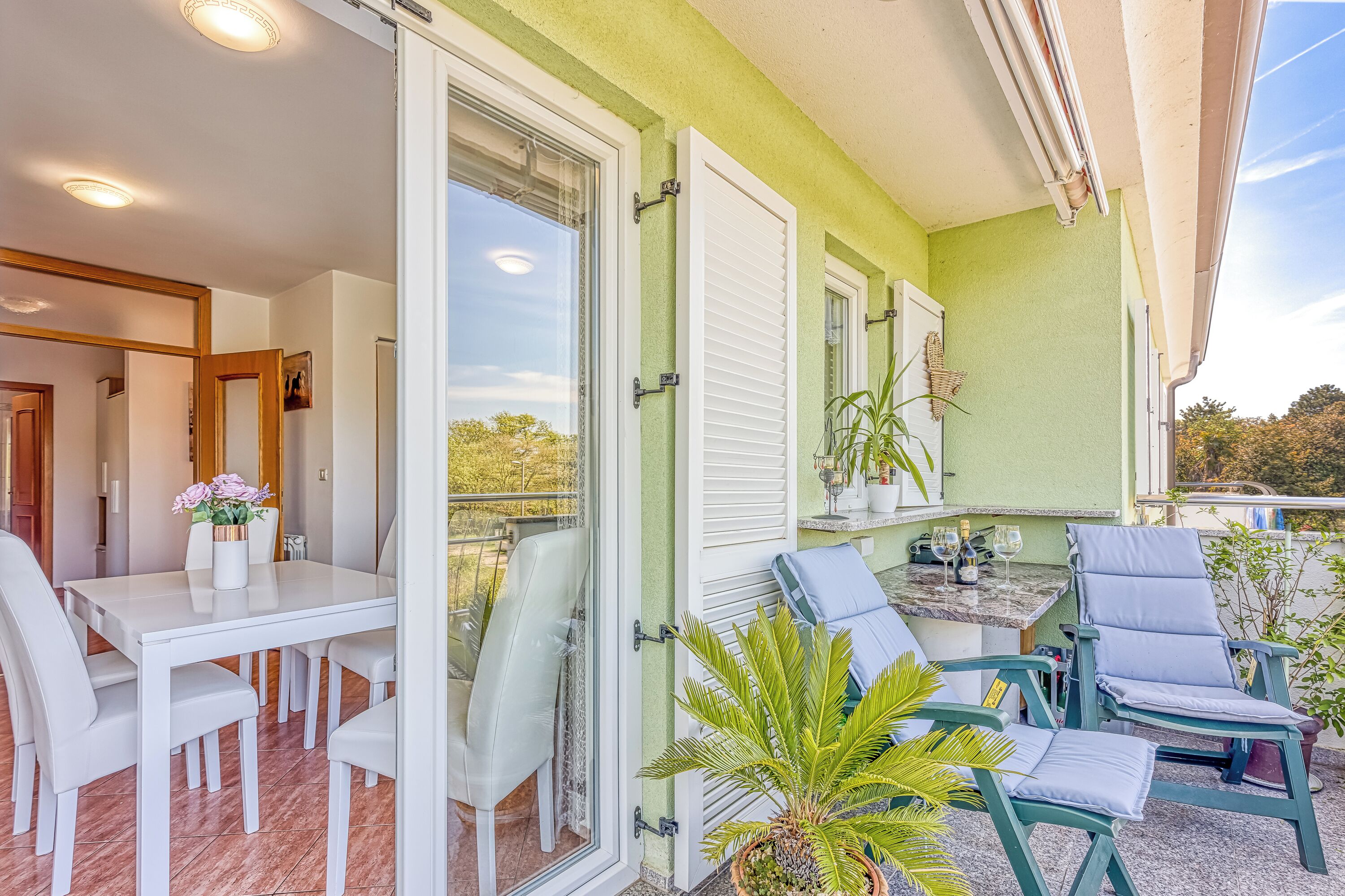 Een balkon met een eettafel en stoelen, een plant in pot en een zithoek met een tafel en stoelen.