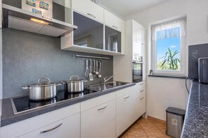Cozinha moderna com bancada preta, eletrodomésticos de aço inoxidável e janela com vista para o verde.