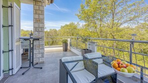 An outdoor balcony with wicker furniture, a bowl of fruit, and a view of trees. - Sea Breeze Residence Mariella (Umag)