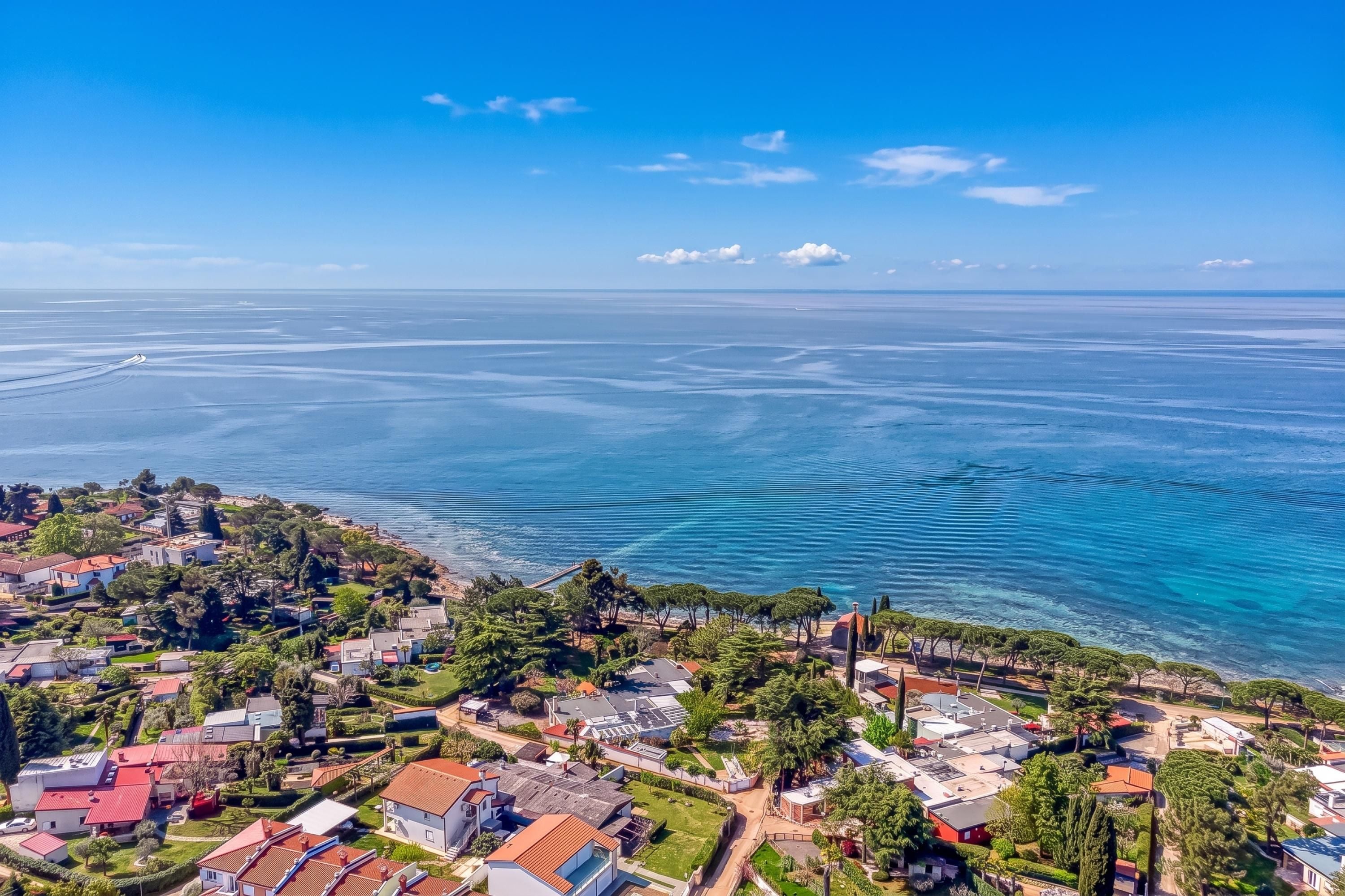 A coastal residential area with houses, trees, and a clear view of the sea.